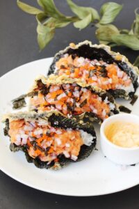 A white plate with 3 sushi tacos with crispy fried seaweed shell.