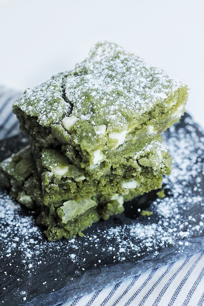 Close up of 3 white chocolate matcha brownies slices on top of each other. 