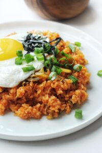 A closeup of Kimchi Fried Rice topped with a fried egg, green onions and roasted seaweed.