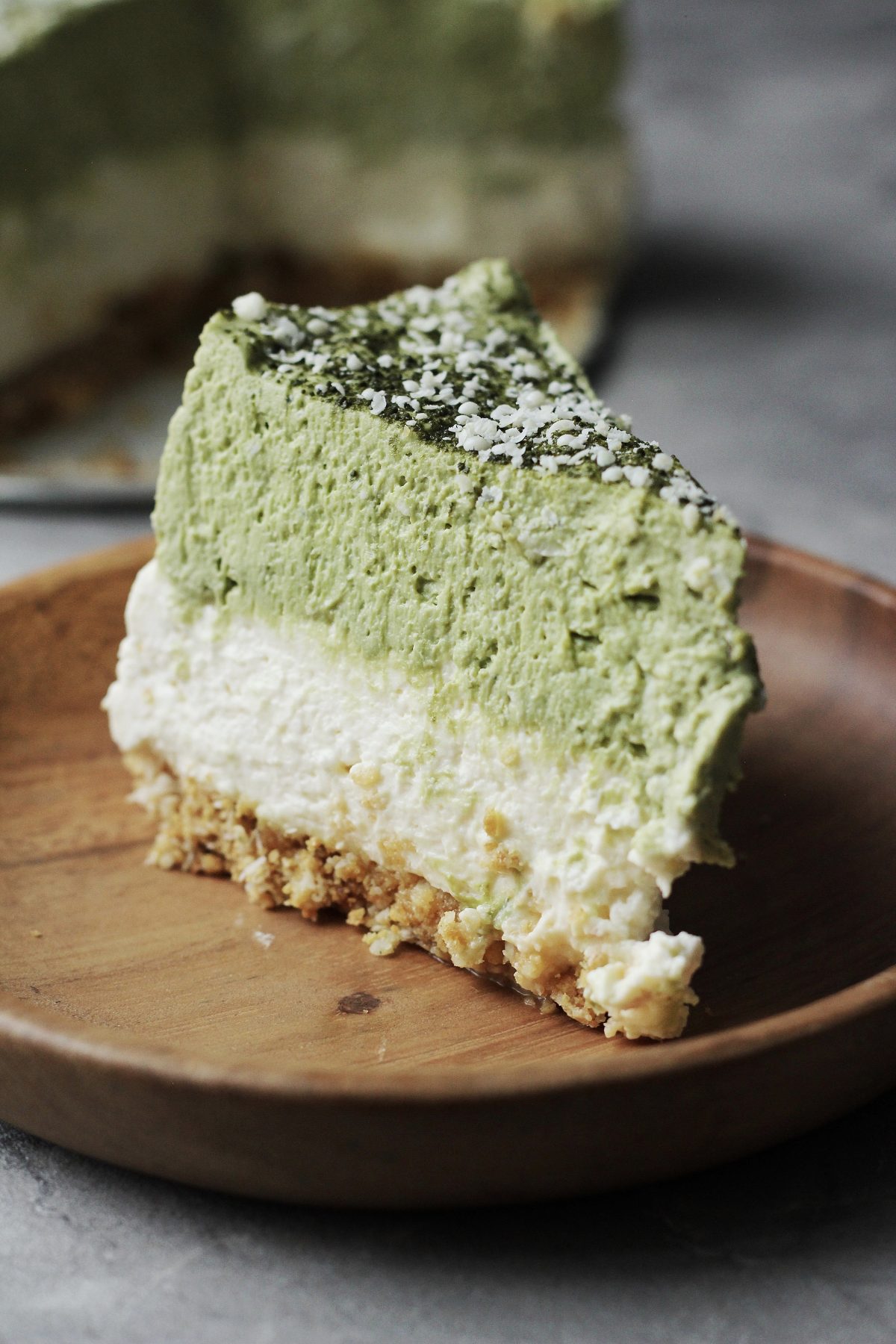 A slice of our no-bake Matcha green tea cheesecake on a wooden plate.