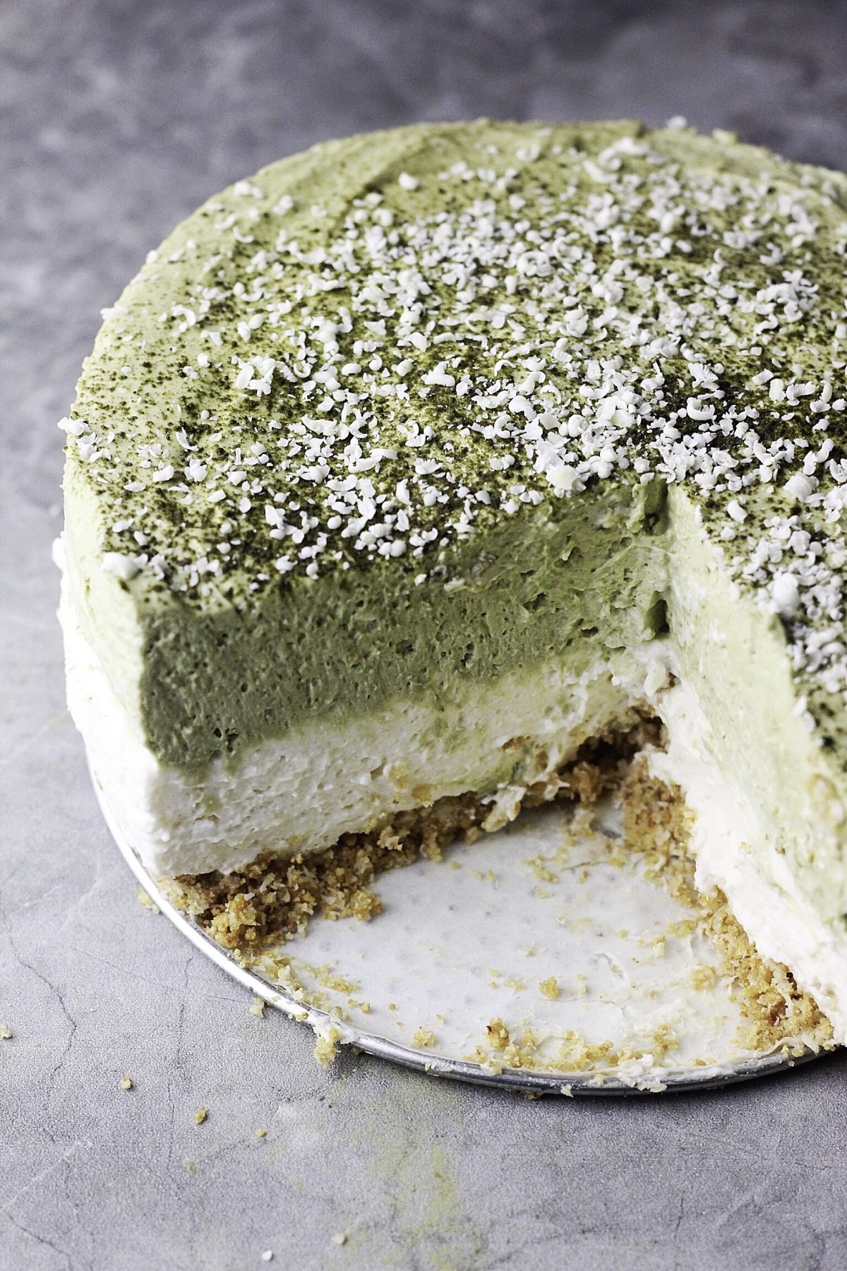 Three quarters of our no-bake matcha (green tea) cheesecake on a gray tile.