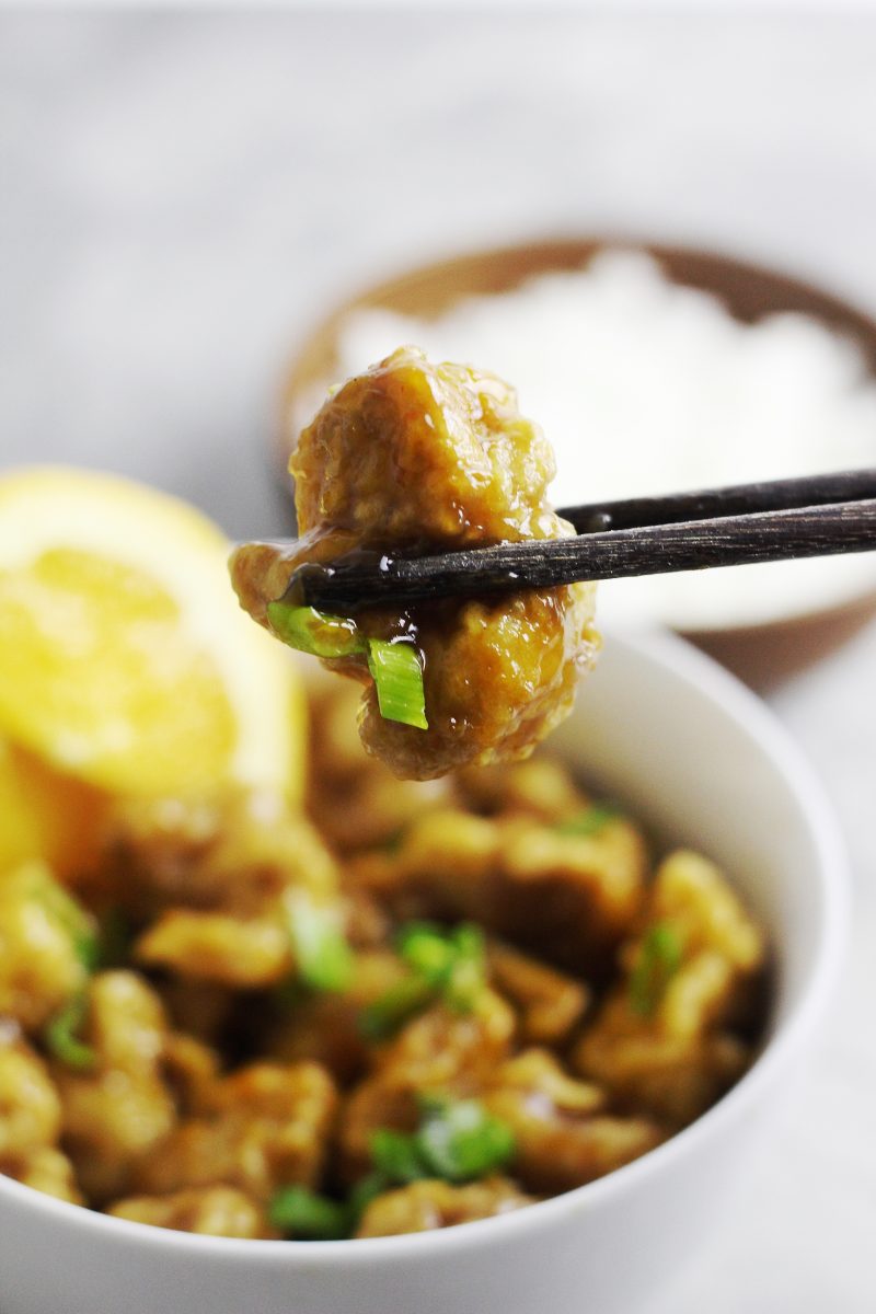 Chopsticks holding a bite-sized Chinese orange chicken.