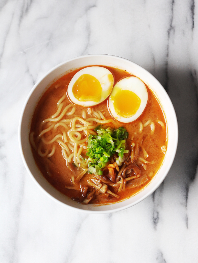 A white bowl filled with spicy garlic miso ramen with 2 egg halves on top.