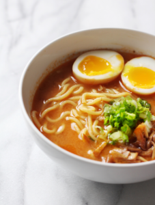 A bowl of spicy garlic miso ramen, topped with an egg and scallions.