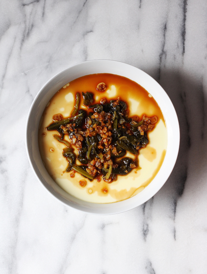 Bowl of Chinese steamed egg topped with garlic and pickled cabbage.