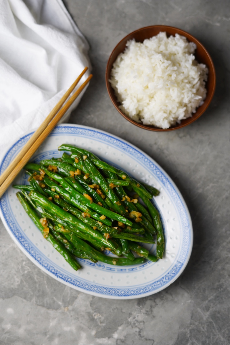 A bird's eye view on a plate of stir-fried Chinese green beans with a bowl of steamed white rice.