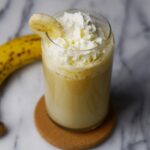 Glass of vegan and dairy free Korean banana milk topped with whipped cream.