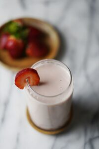 A glass of strawberry milk with a plate of strawberries