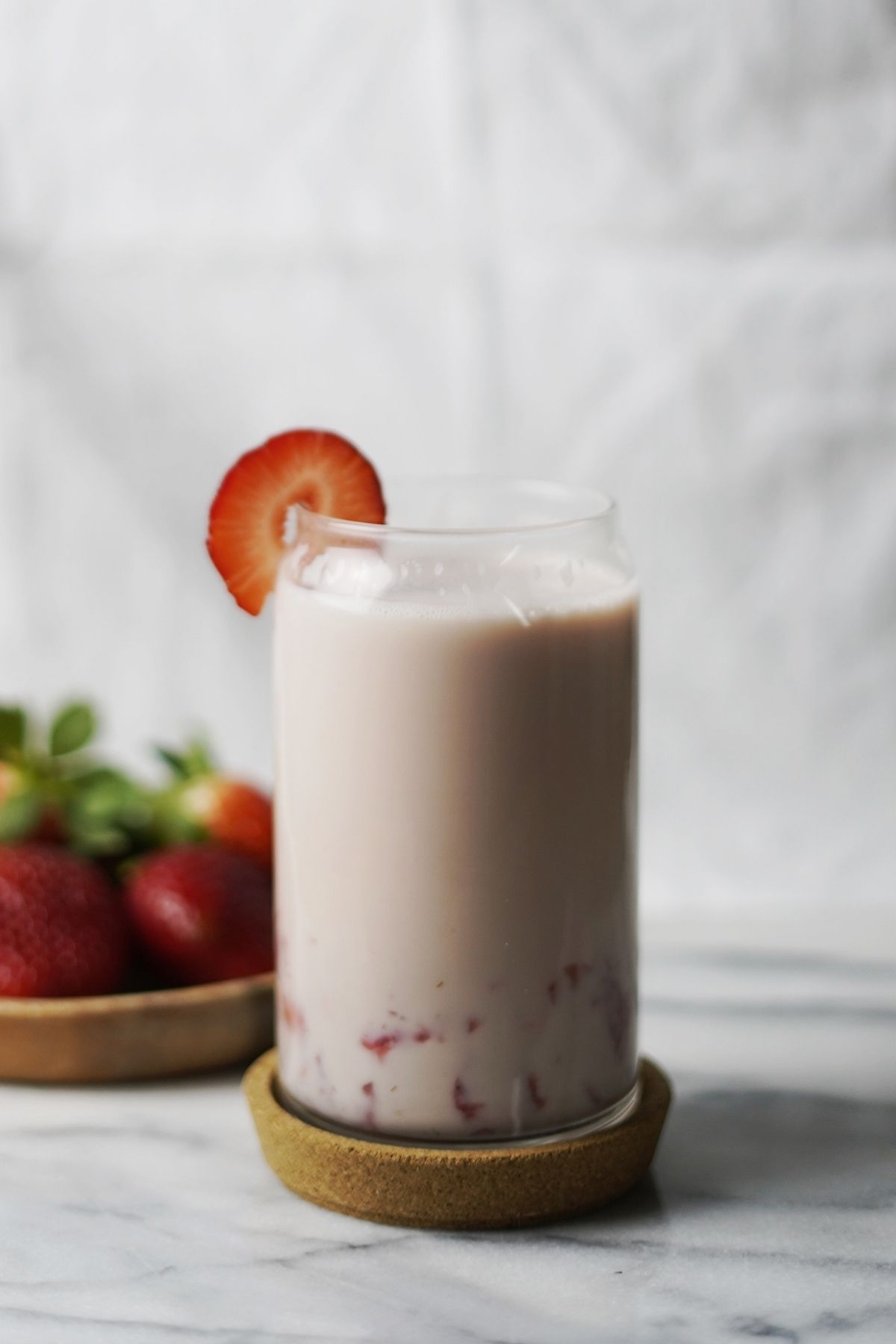 A glass of vegan Korean strawberry milk with a plate of strawberries