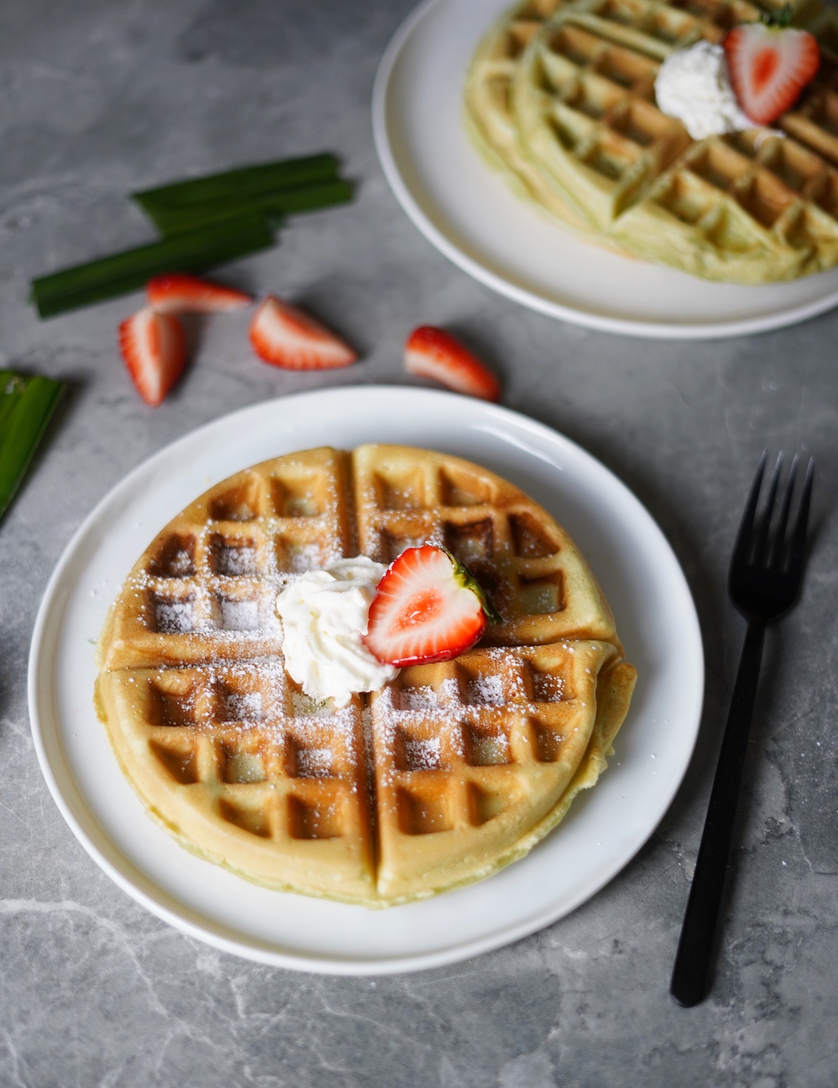 A plate with a crispy and chewy pandan waffle topped with strawberries and whipped cream.