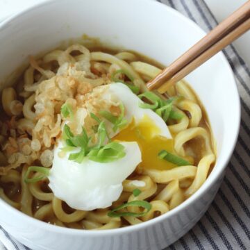 Bowl of curry udon with pierced poached egg.