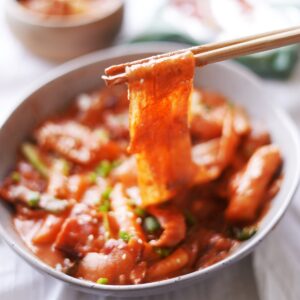 Chopsticks lifting the spicy cramy thick glass noodles and rice cakes.