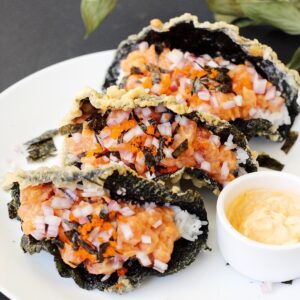 3 sushi tacos with crispy fried seaweed shells on a plate with a side of spicy mayo.