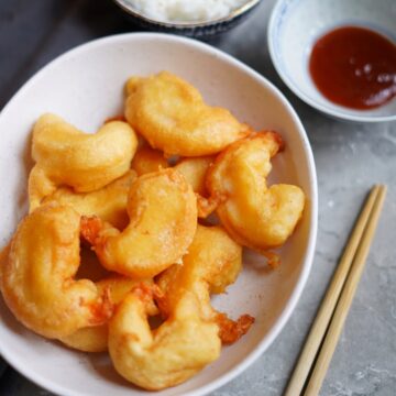 Bowl of Chinese fried shrimps with a side of sweet and sour sauce.