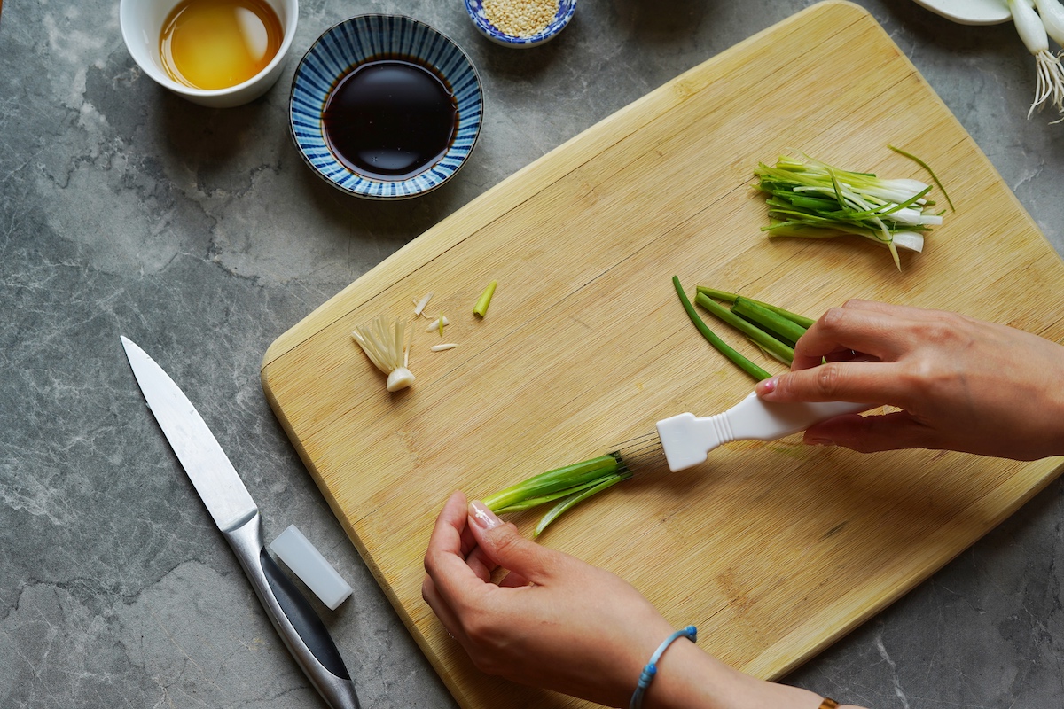 Hands demonstrating how to slice green onions with a slicer.