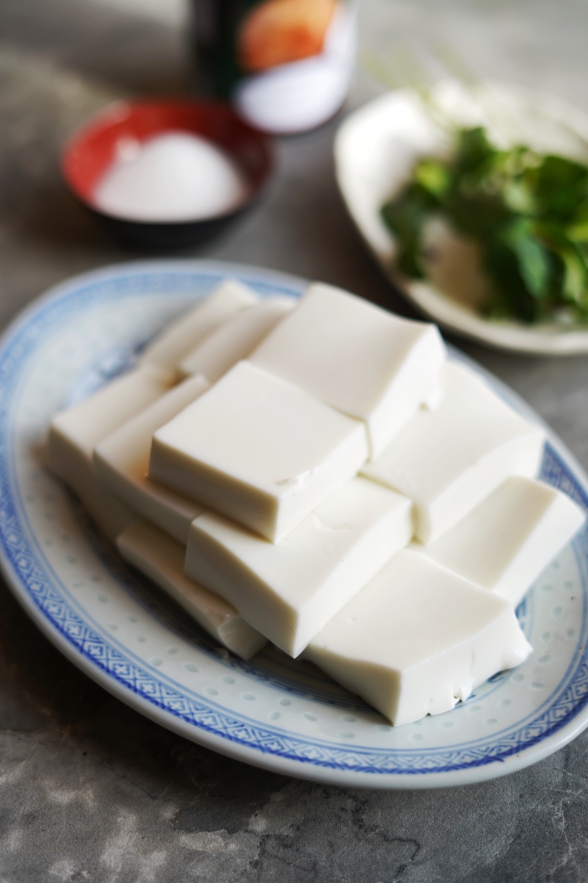 Front side view of coconut jelly cut into squares stacked on top each other with sugar and mint served on a plate.