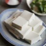 Close up front view of coconut jelly cut into squares stacked on top of each other served on a plate.