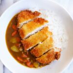 Bird's view of chicken katsu curry served with steamed rice in a white bowl on a marble table.