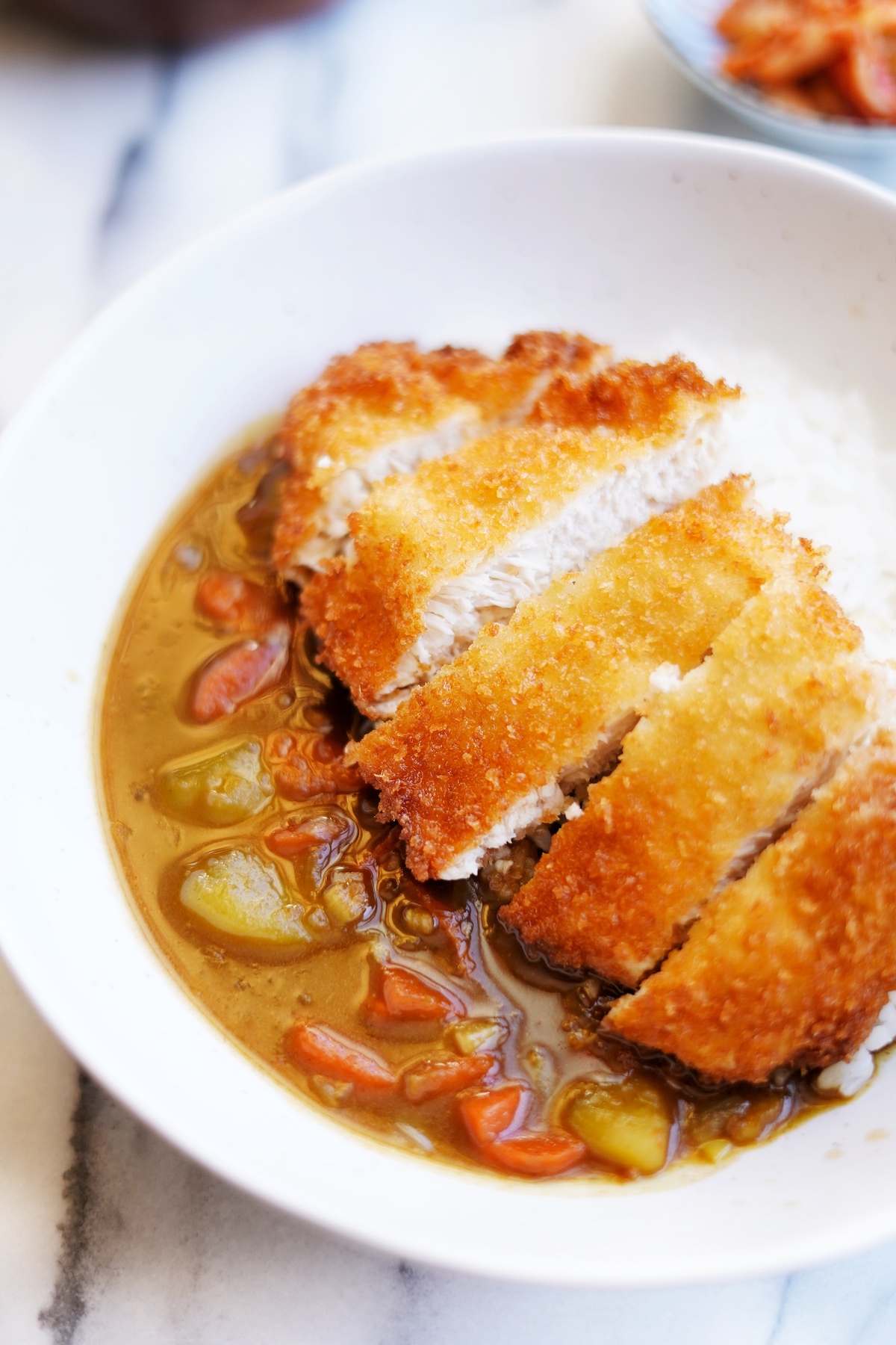 Close up front view of fried chicken cutlet cut into strips served with steamed rice and Japanese curry sauce.