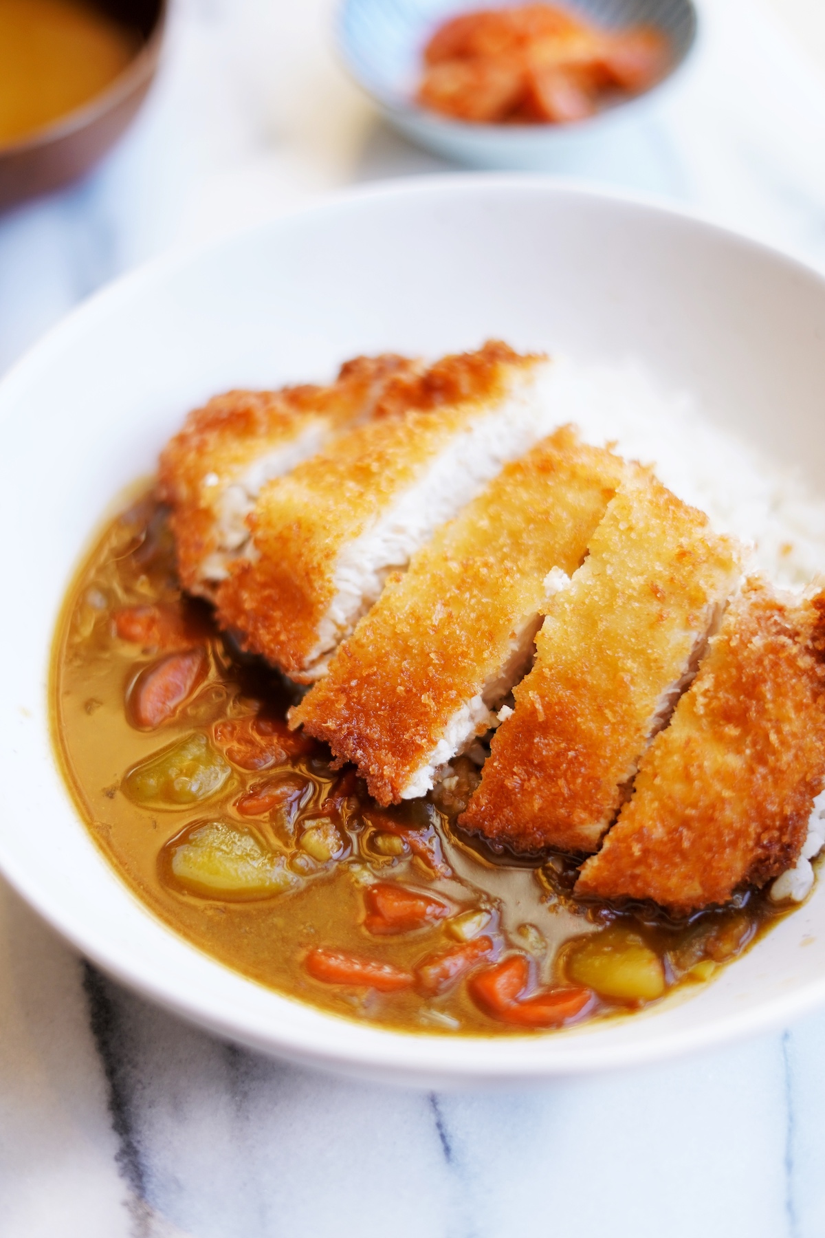 Close up front view of chicken katsu curry served in a white bowl on marble table.